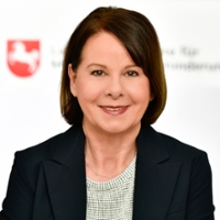 Portraitfoto von Ina Hoffmann-Glaß: Eine lächelnde Frau mit Brille und kurzem brünetten Haarschnitt Portraitfoto von Ina Hoffmann-Glaß: Eine lächelnde Frau mit Brille und kurzem brünetten Haarschnitt